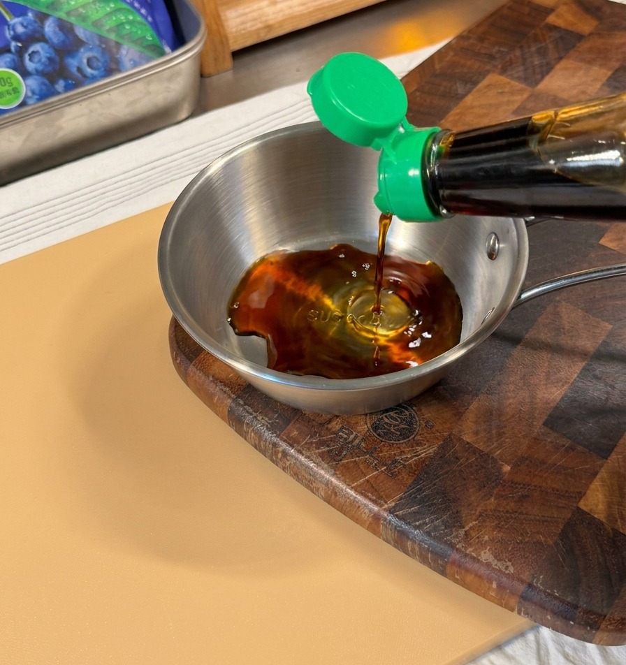 Dunkle Sojasauce wird aus einer Flasche in eine kleine Edelstahlschüssel gegossen.