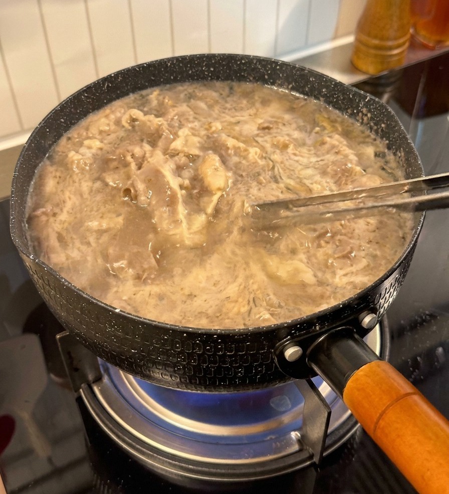 Rindfleischscheiben werden mit einer Zange aus dem Wasser gehoben und sehen hell und vorgegart aus.