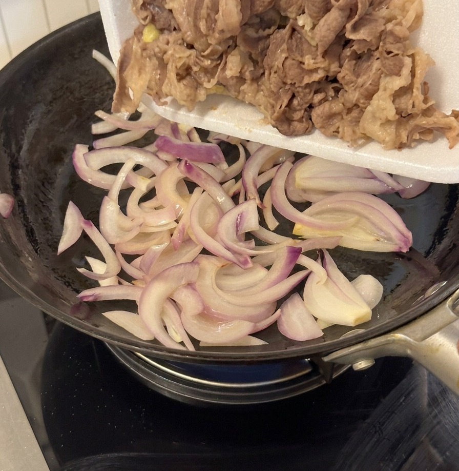 Blanchiertes Fleisch wird aus einer weißen Schale in die Pfanne zu den Zwiebeln gegeben.