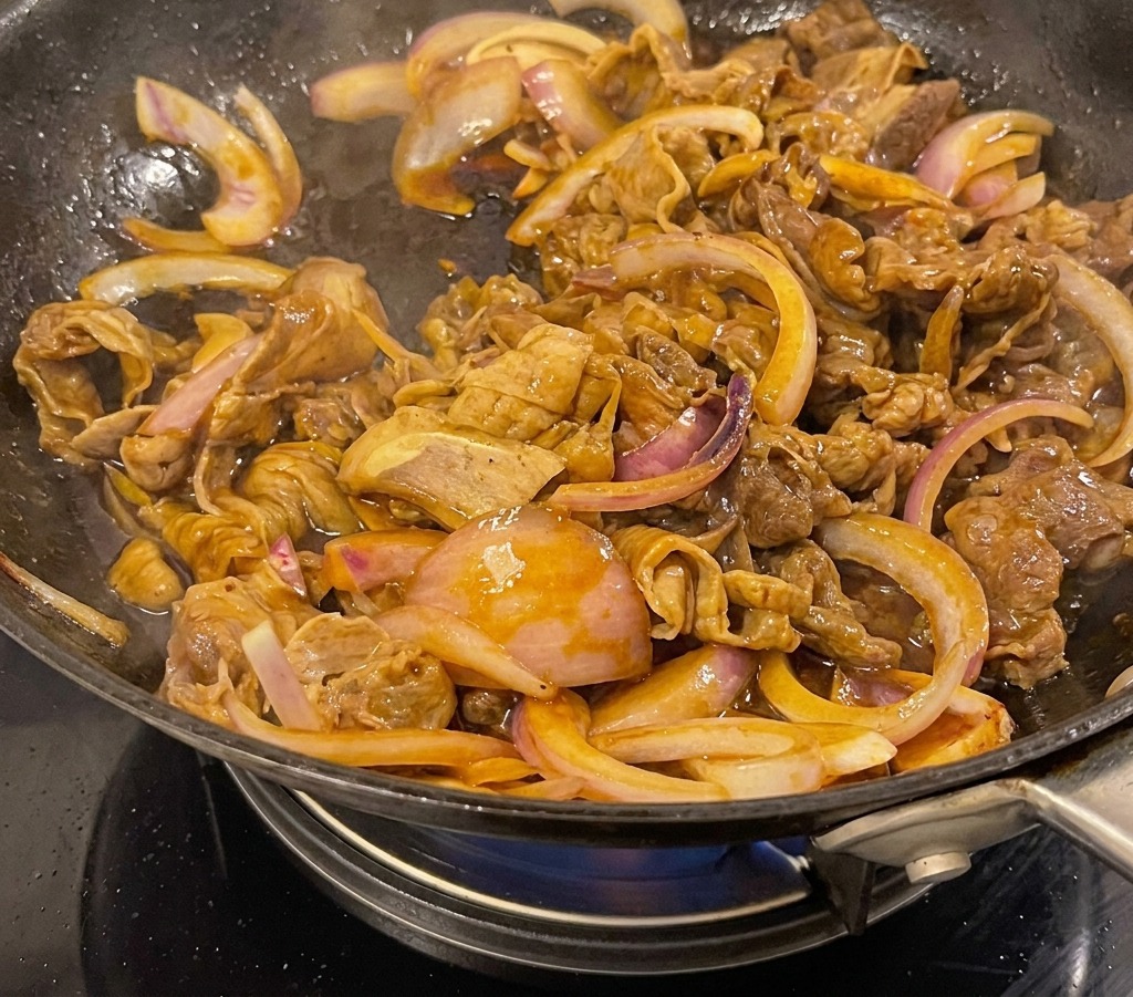 Rindfleisch und Zwiebeln köcheln in einer dicken, dunkelbraun glänzenden Sauce in einem Wok.