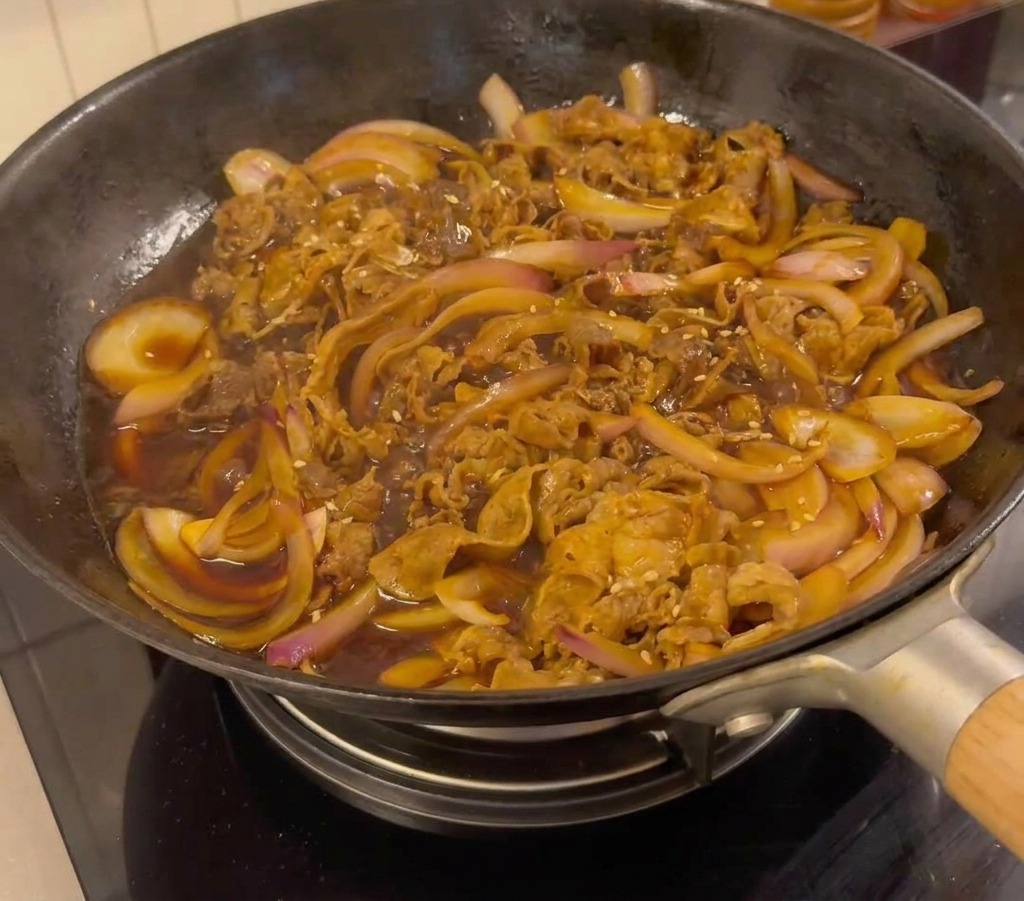 Fertiges Rindfleisch in der Pfanne, garniert mit Sesam und geschnittenen Frühlingszwiebeln.