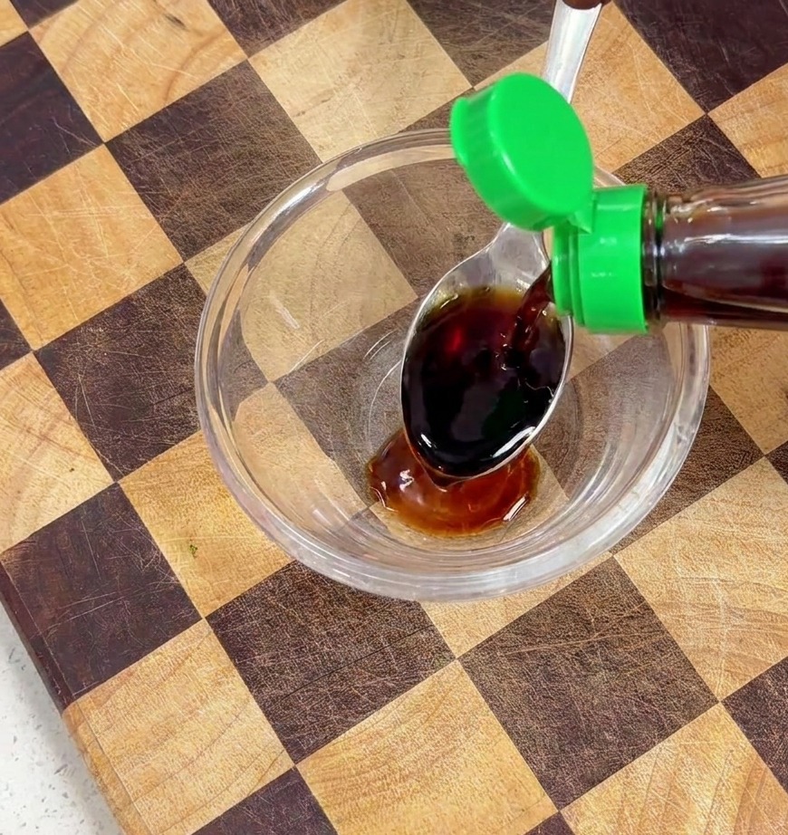 Dunkle flüssige Würze wird aus einer Flasche in eine Glasschale mit Sojasauce gegossen.