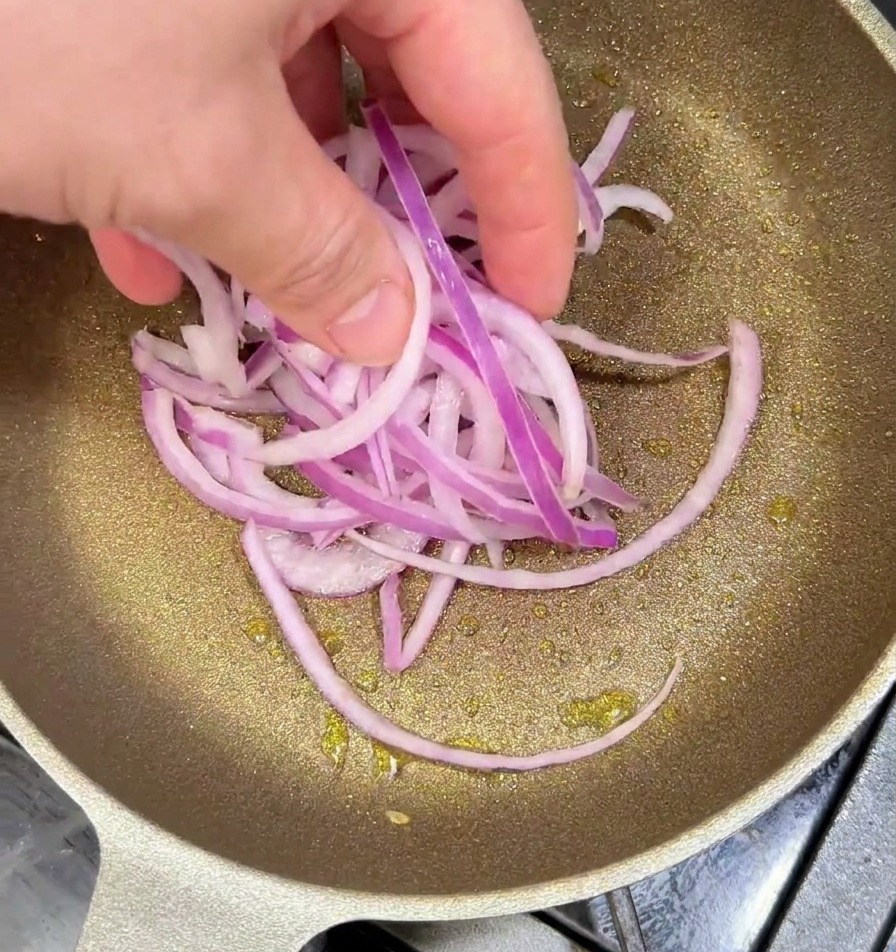 Geschnittene lila Zwiebeln werden von Hand in eine erhitzte Pfanne mit Öl gegeben, um sie glasig anzubraten.