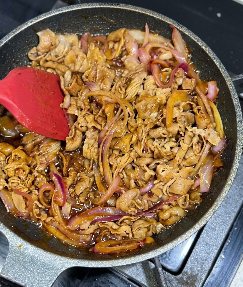 Dünne Rindfleisch- und Zwiebelstreifen werden in einer Pfanne mit einer dicken, schimmernden braunen Glasur geschwenkt.