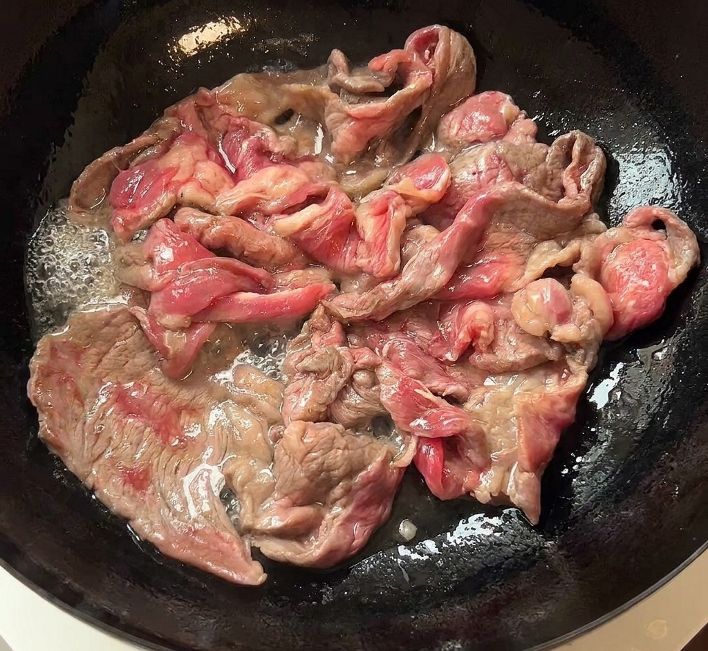 Gebräuntes Fleisch wird aus der Pfanne auf einen weißen Teller gelegt.