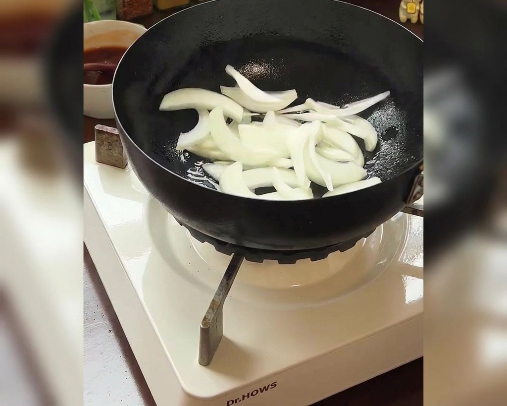 Zwiebelstreifen in der Pfanne mit einer Schüssel Kimchi im Hintergrund.