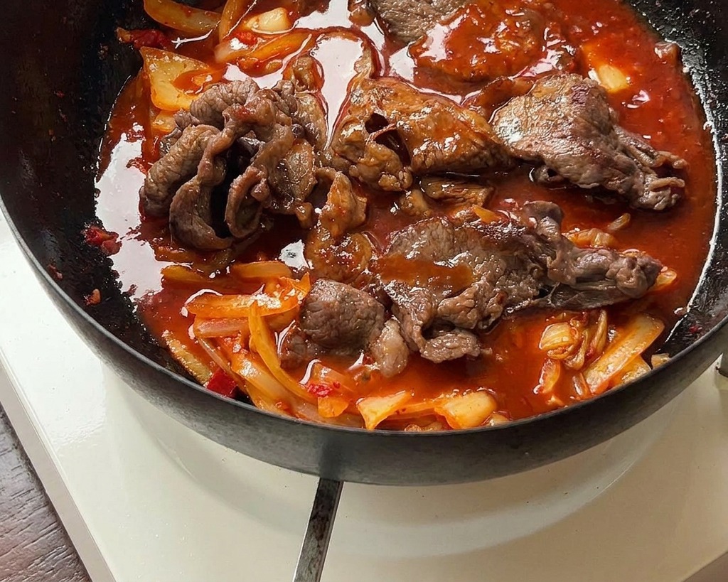 Fleisch und Kimchi köcheln in einer glänzenden roten Sauce.