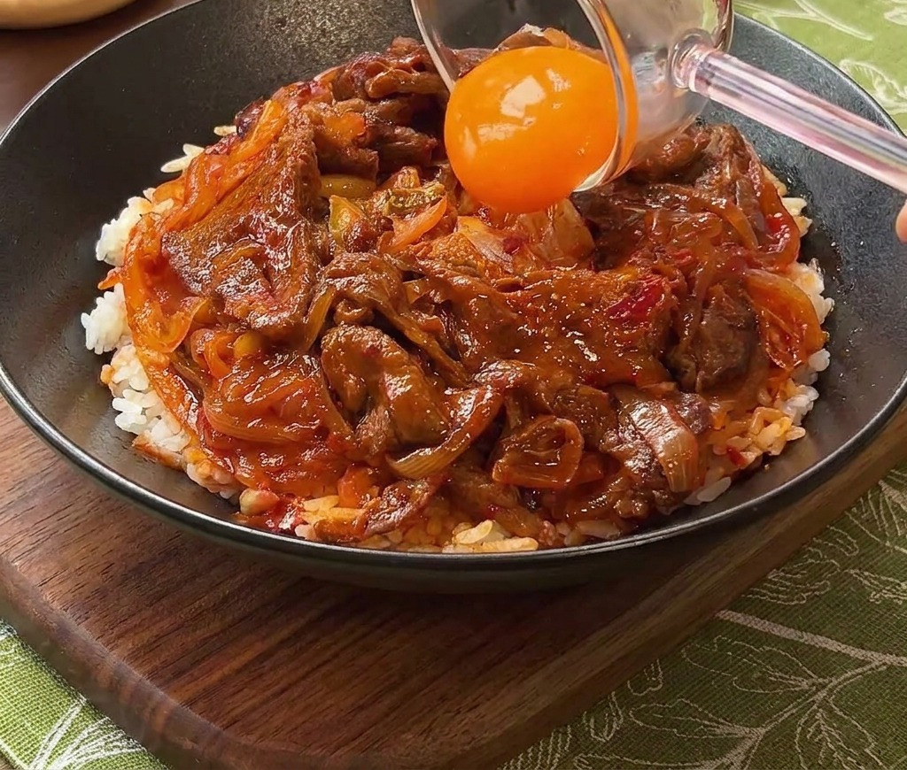 Ein Eigelb wird vorsichtig in die Mitte der Fleisch-Reis-Schüssel gesetzt.