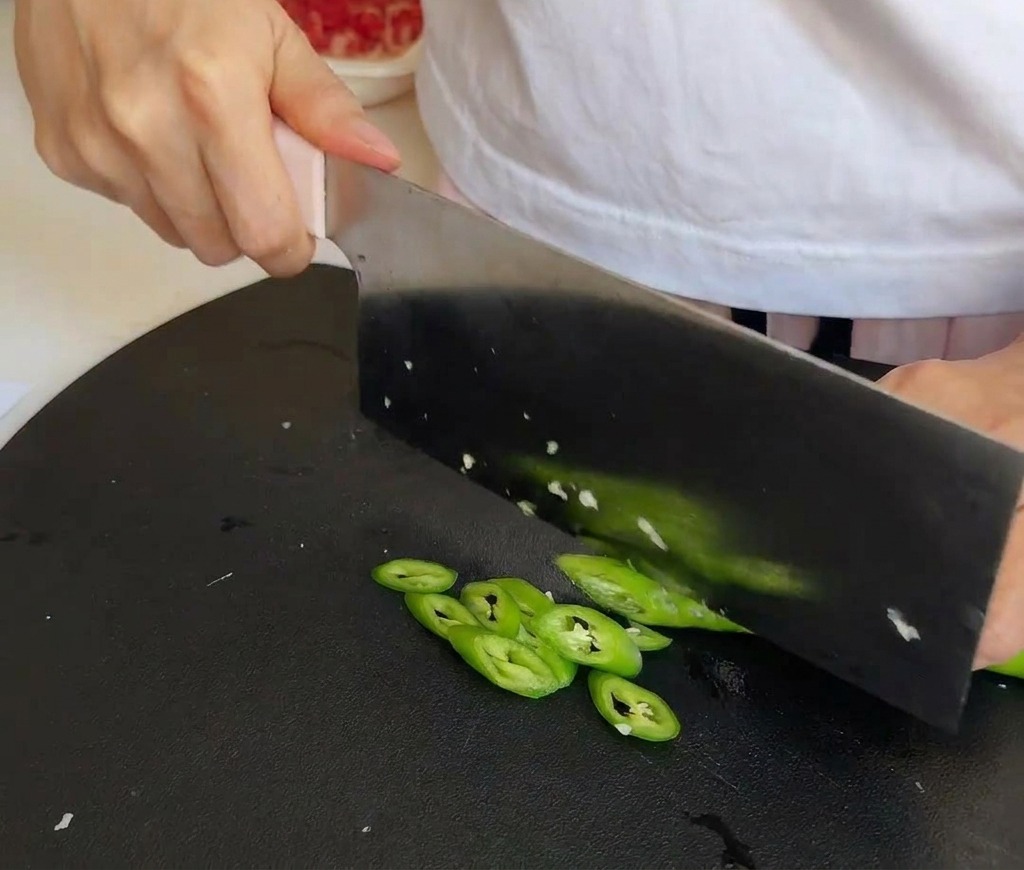 Frische grüne Chilischoten werden auf einem Schneidebrett in feine Ringe geschnitten.