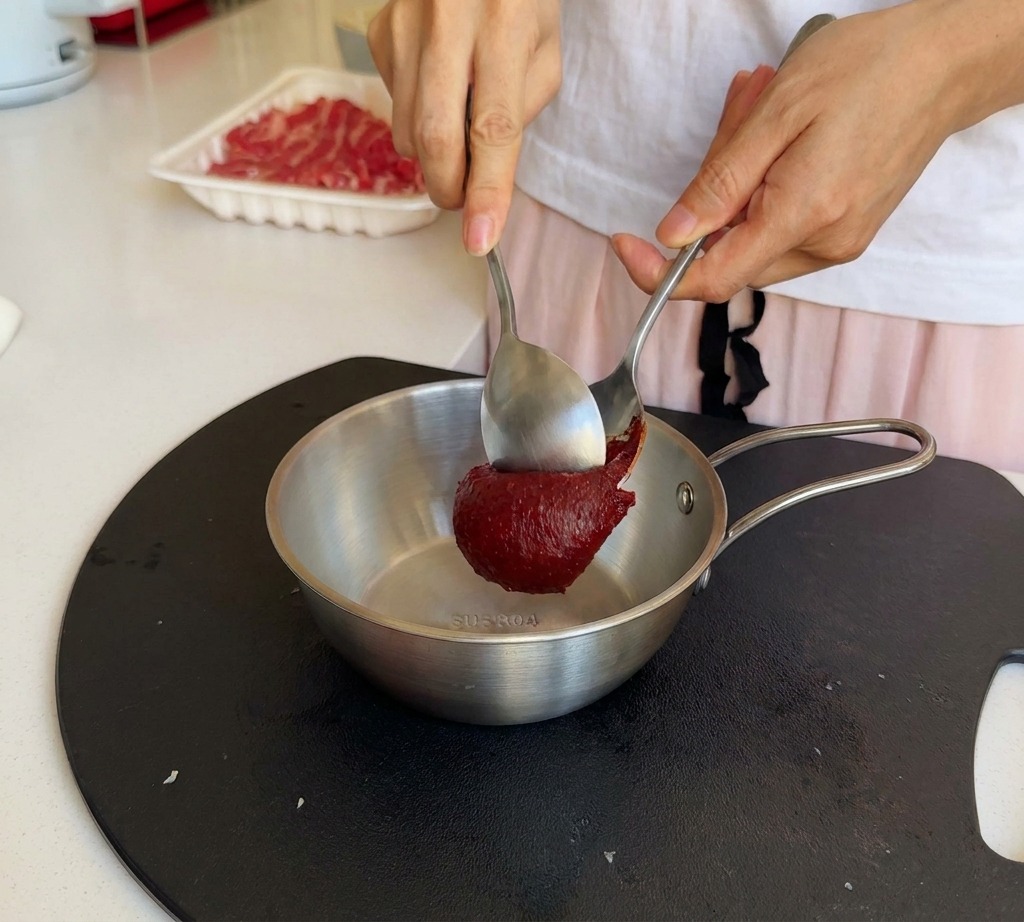 Ein Löffel tiefrote koreanische Chilipaste wird in eine Schüssel mit Sojasauce gegeben.