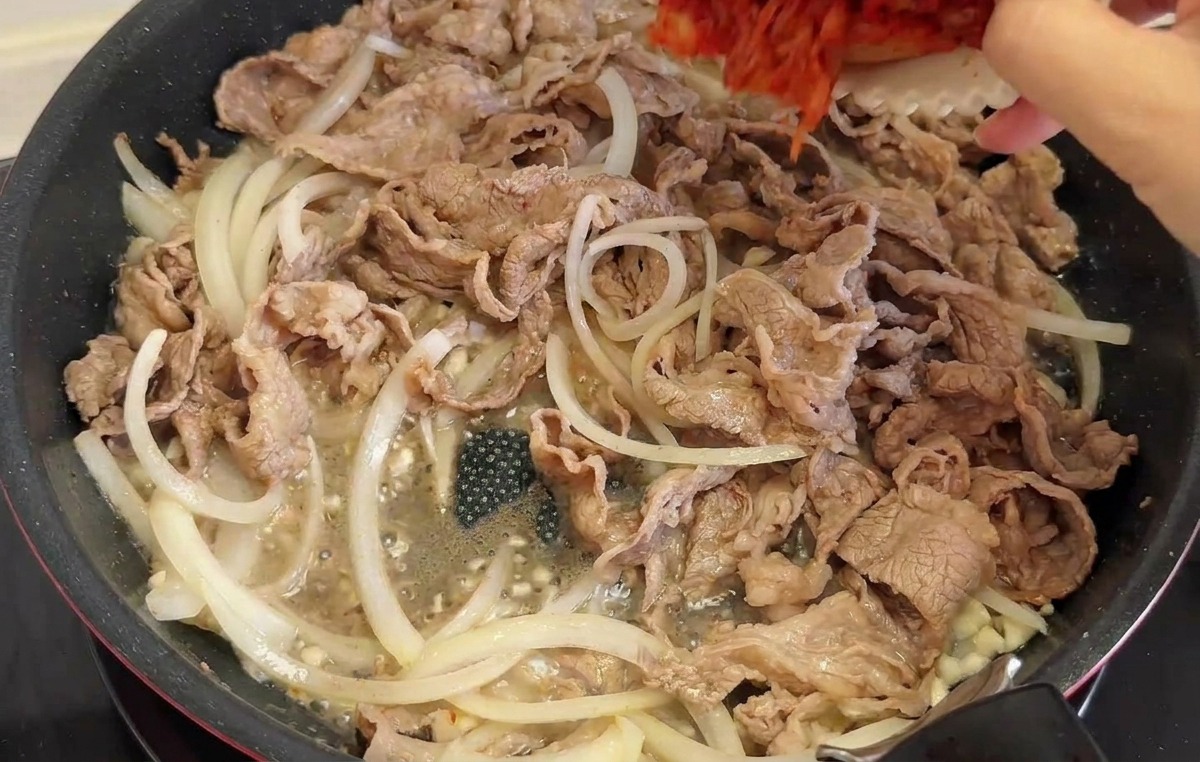Gehacktes rotes Kimchi und grüne Chiliringe werden in die Pfanne zum Fleisch und den Zwiebeln gegeben.