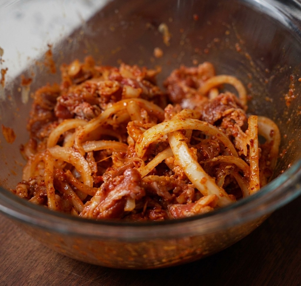 Dünn geschnittenes Rindfleisch, weiße Zwiebeln und rote Chilipaste, gründlich in einer Glasschüssel vermischt und bereit zum Marinieren.