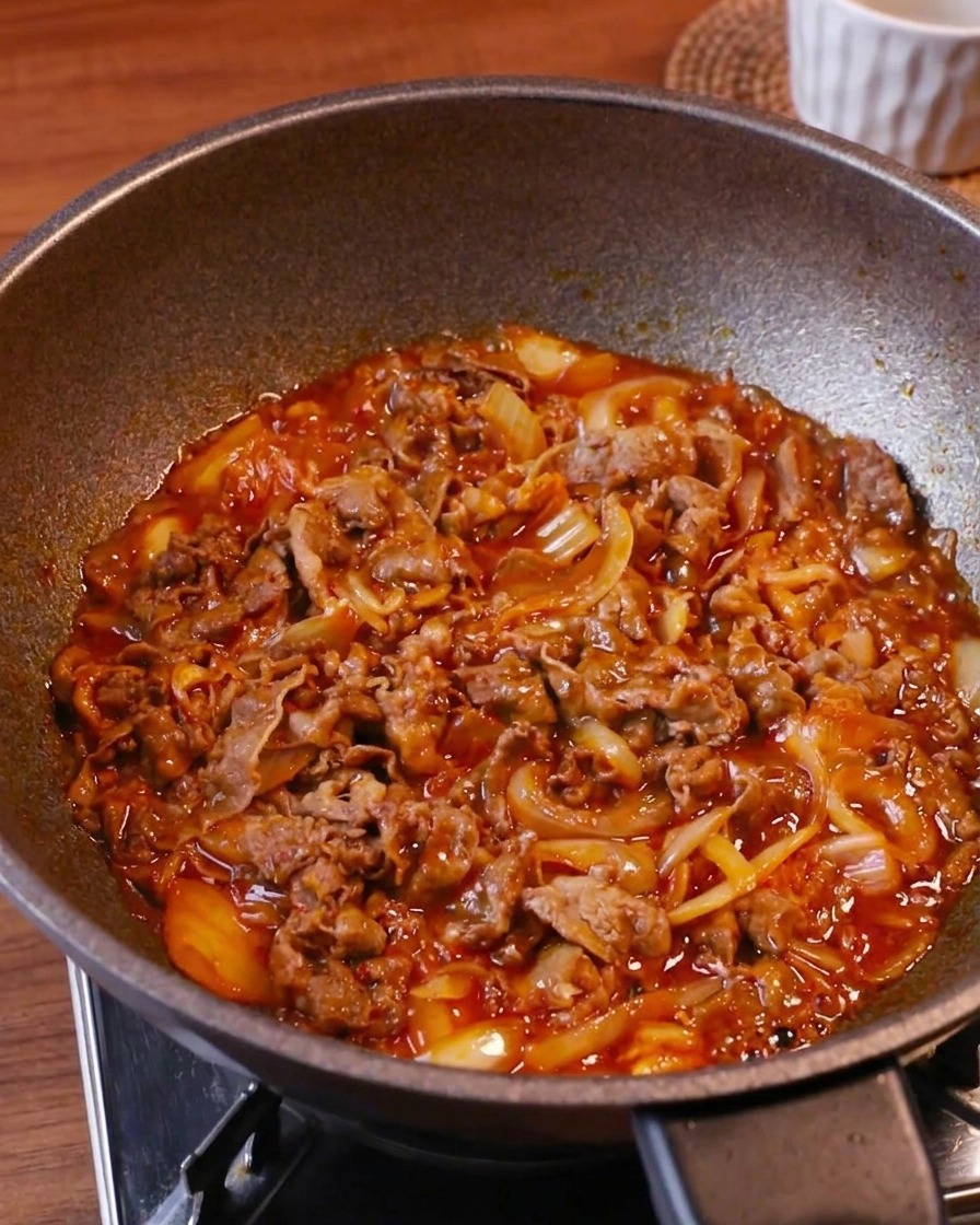 Zartes Rindfleisch, Kimchi und Zwiebeln köcheln in einer glänzenden roten Sauce bei hoher Hitze in einem Wok.