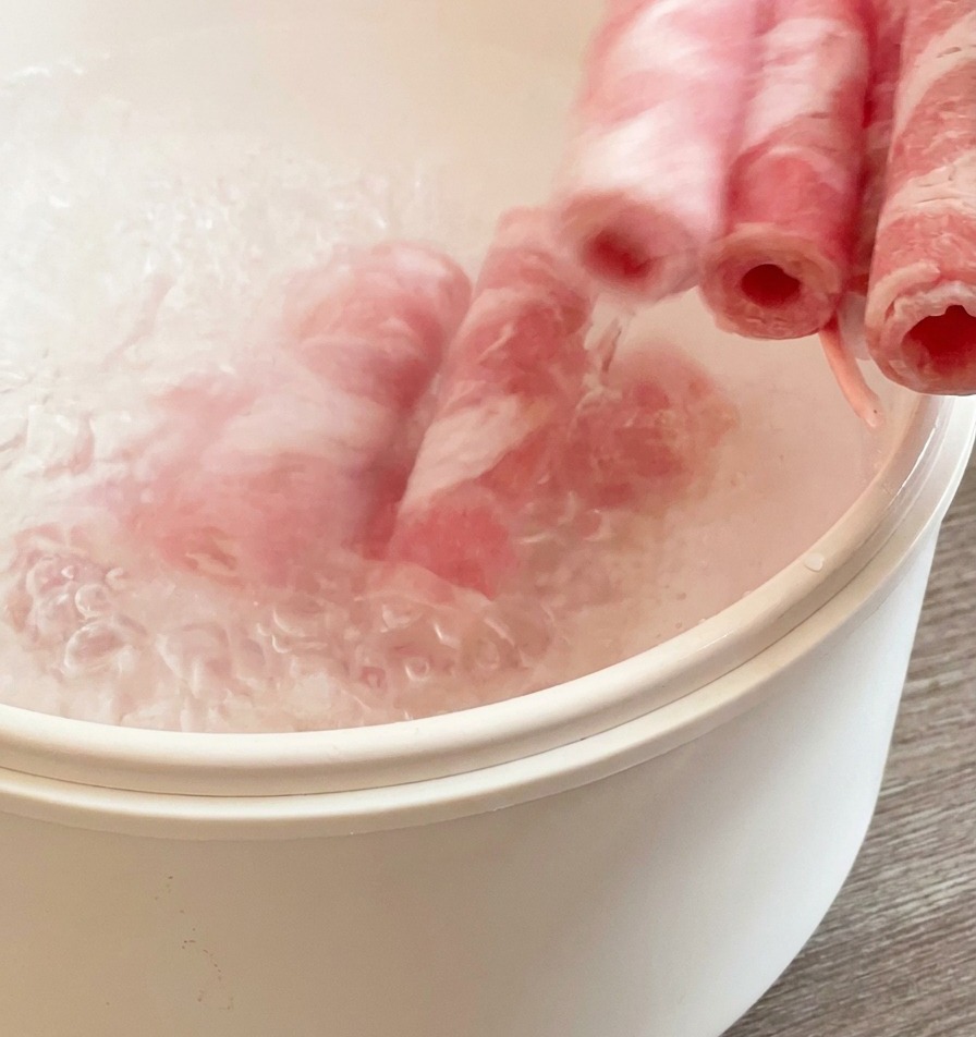 Gefrorene Rindfleischrollen werden in einem weißen Topf mit kochendem Wasser kurz blanchiert.