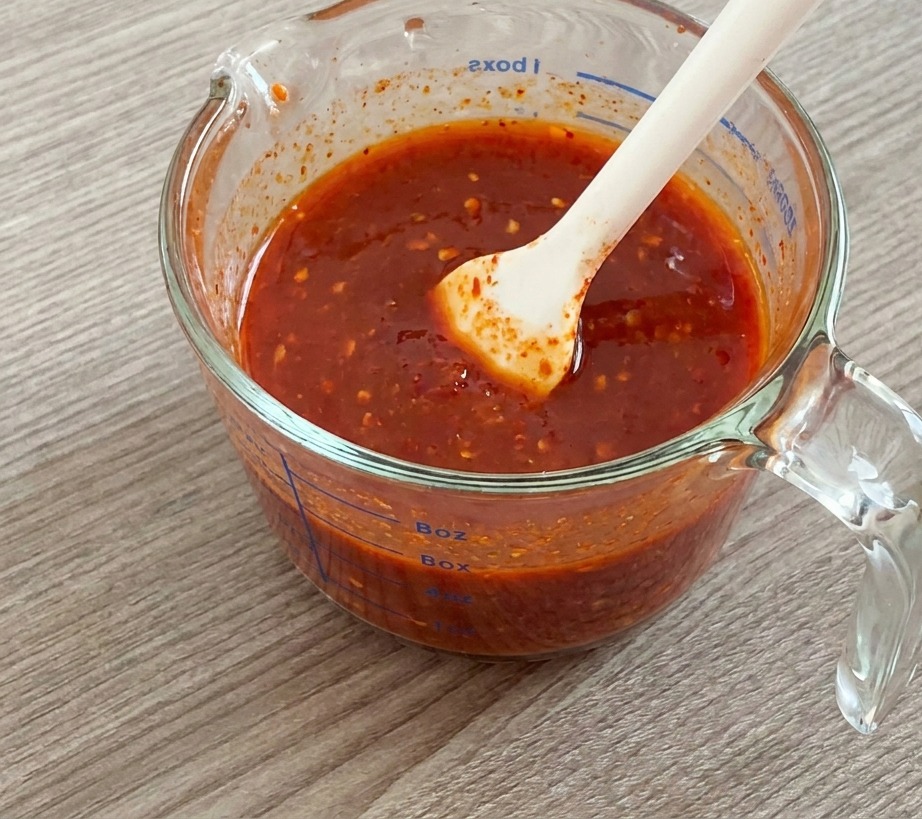 Ein weißer Silikonspatel rührt eine dicke rote Sauce in einem Glasmessbecher an.