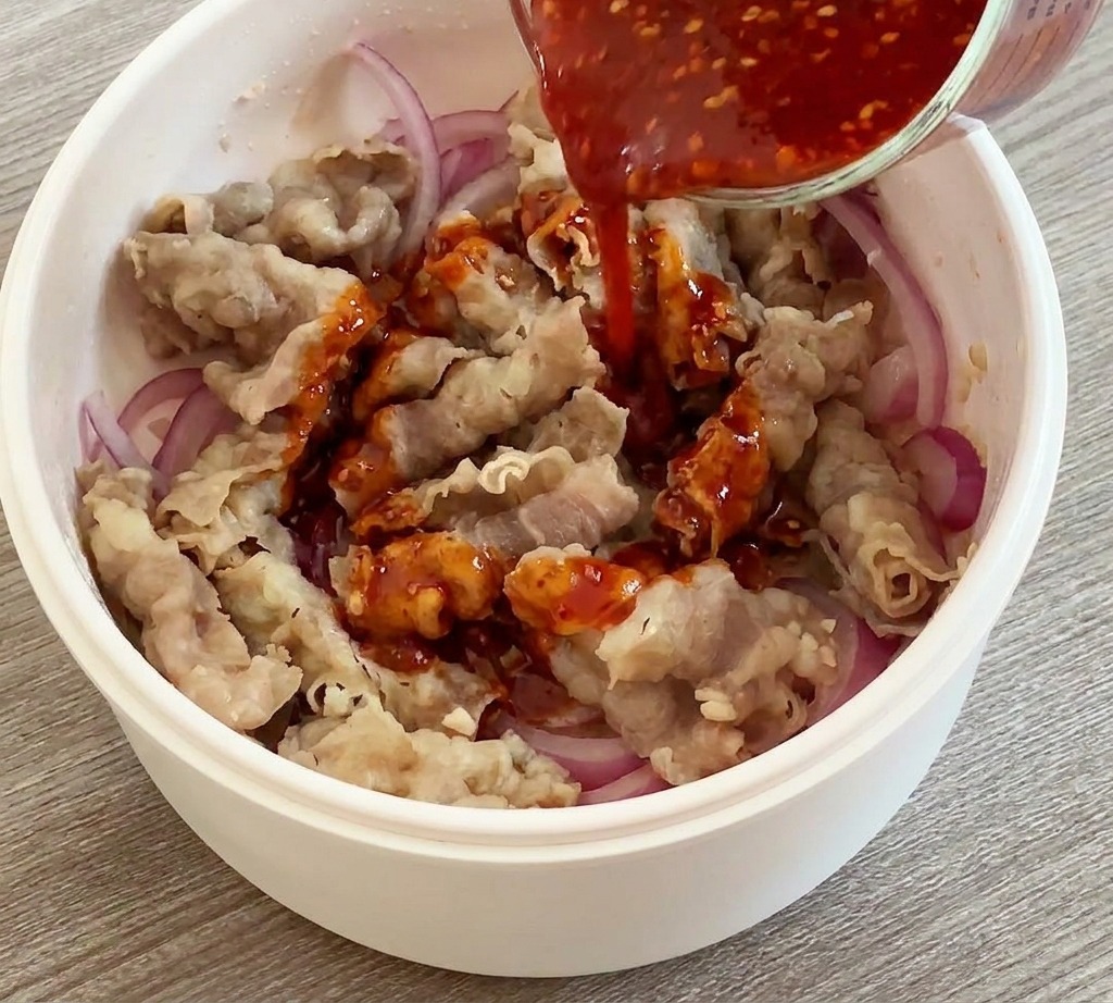 Rote Sauce wird aus einem Messbecher über gebratenes Fleisch und Zwiebeln gegossen.