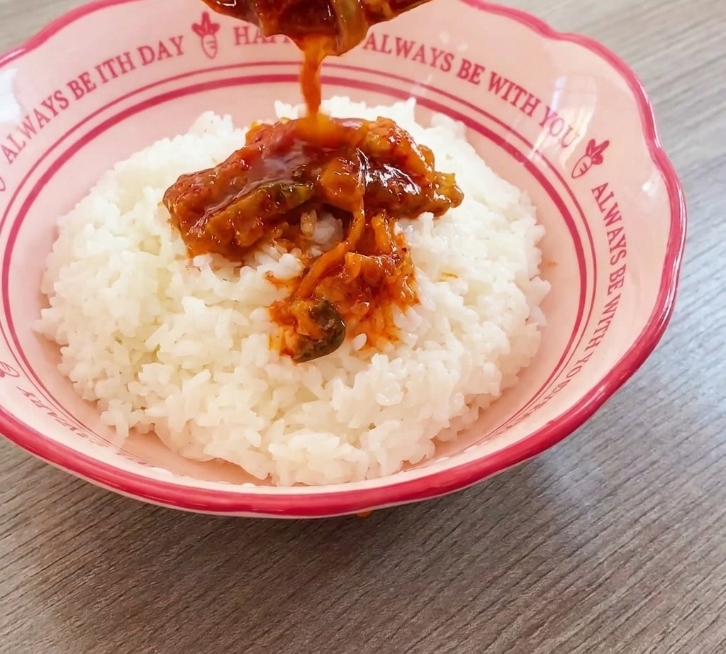 Die Kimchi-Fleisch-Mischung wird mit einem Löffel auf eine Schüssel mit weißem Reis gegeben.