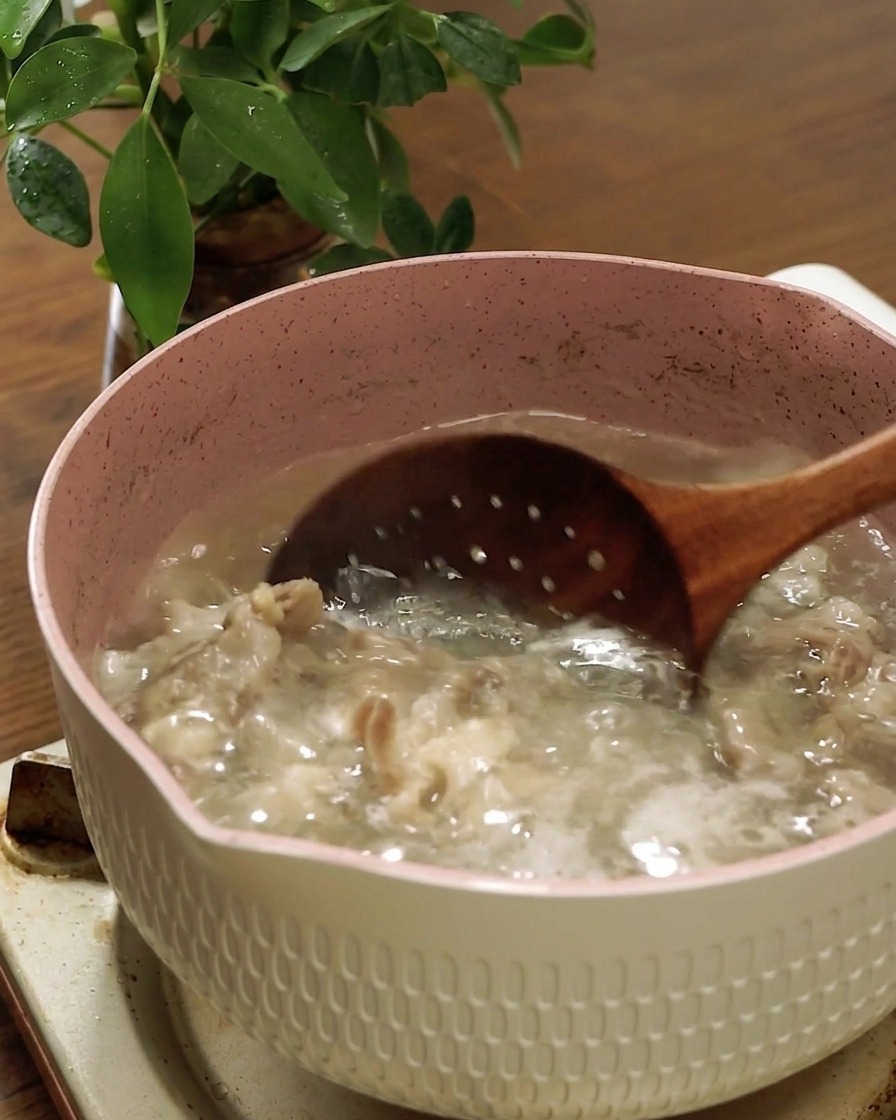 Ein Schaumlöffel aus Holz hebt das gegarte Rindfleisch aus dem kochenden Wasser.