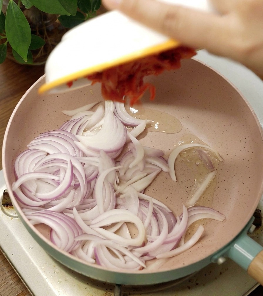 Eine rosa Keramikpfanne mit roten Zwiebelstreifen und scharfem roten Kimchi.
