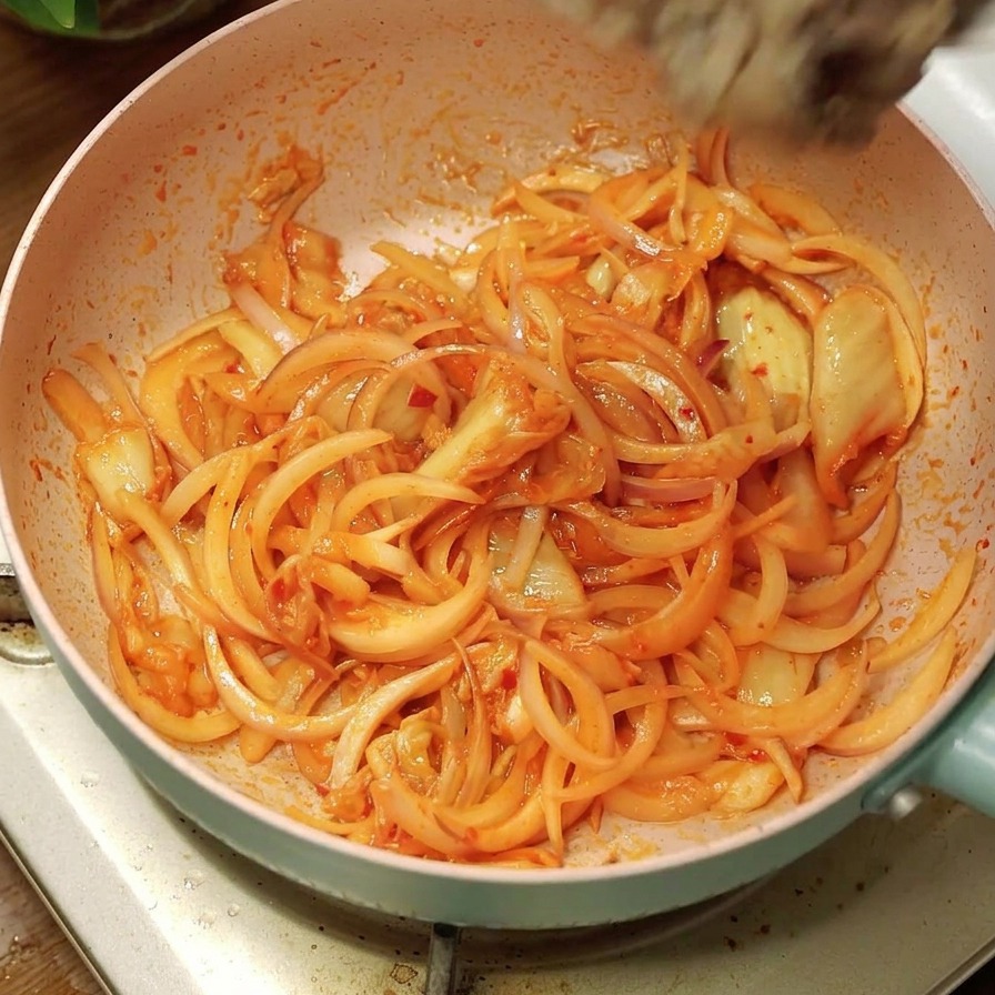 Vorgegartes Rindfleisch wird aus einer Schüssel in die Pfanne zu den Zwiebeln und dem Kimchi gegeben.
