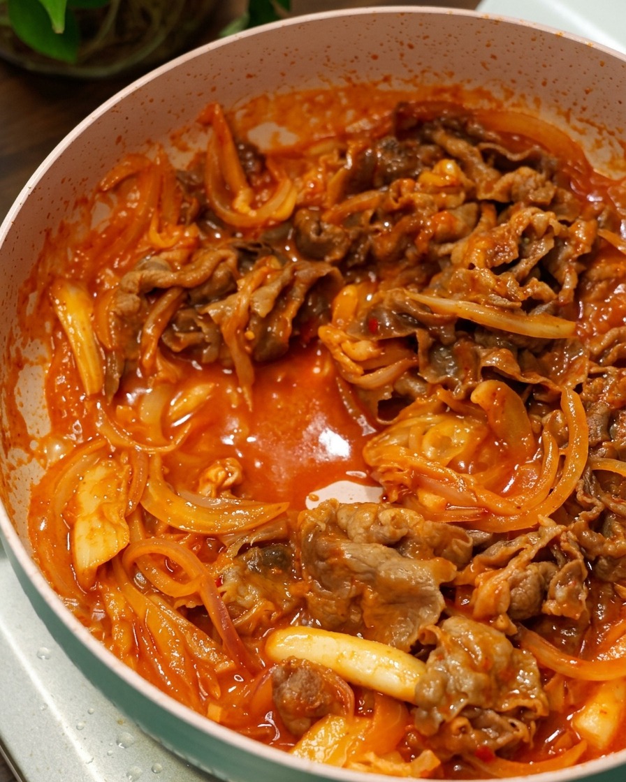 Rindfleisch und Zwiebeln brutzeln in einer glänzenden roten Sauce in der Pfanne.