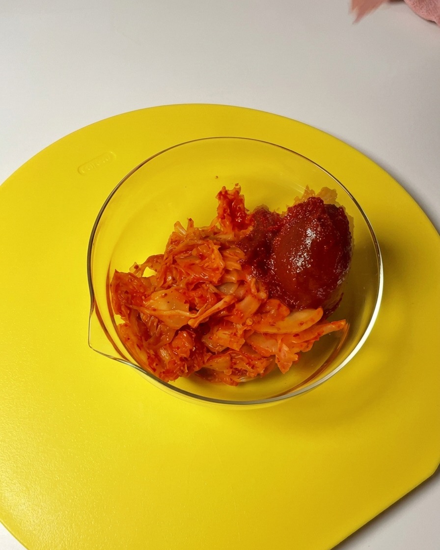 Ein Löffel rotes Gochujang und Chilipulver werden in eine Glasschüssel mit gehacktem Kimchi gegeben.