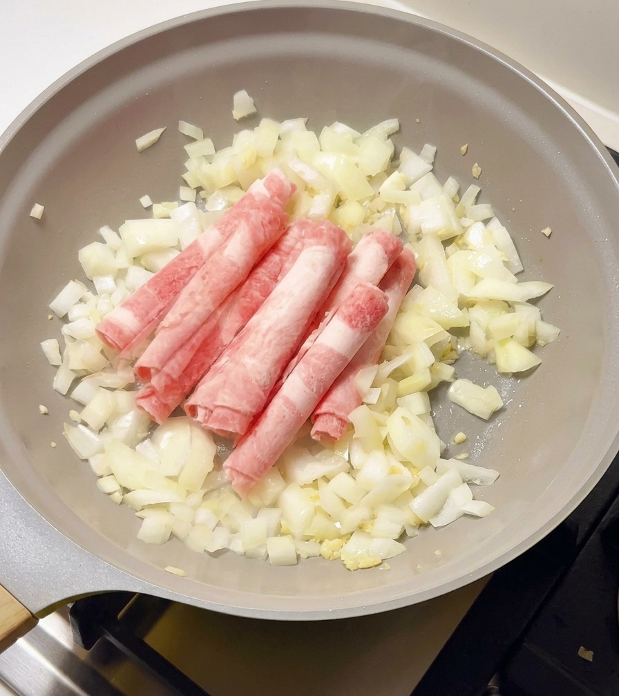 Dünne, gefrorene Rindfleischröllchen werden in die Pfanne zu den glasigen Zwiebeln gegeben.