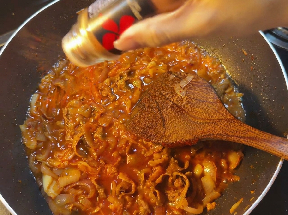 Rotes Chilipulver wird über eine köchelnde rote Sauce mit Rindfleisch und Zwiebeln gestreut.