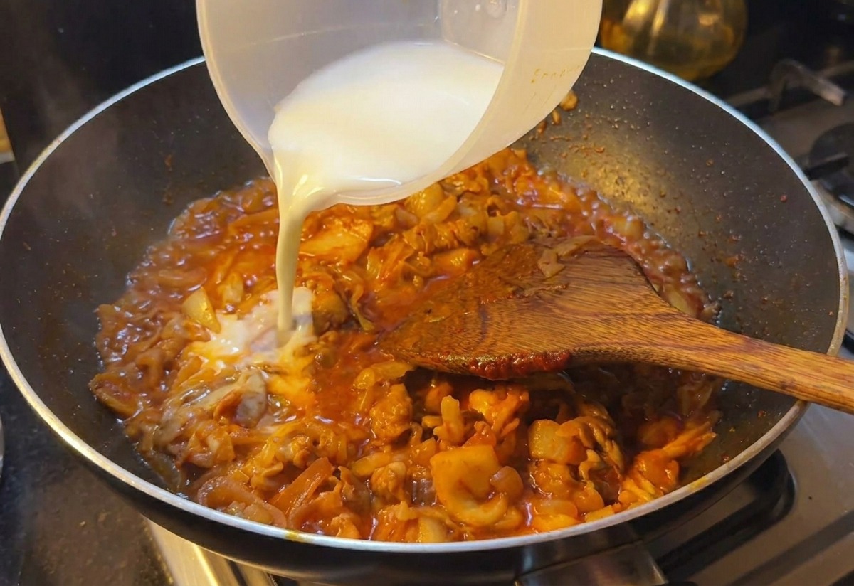 Milchig-weißes Stärkewasser wird in eine Pfanne mit köchelndem Rindfleisch und Kimchi gegossen.
