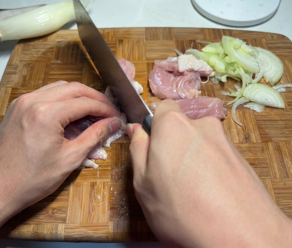 Ein Koch schneidet rohes Hähnchenfleisch in mundgerechte Stücke auf einem Schneidebrett.