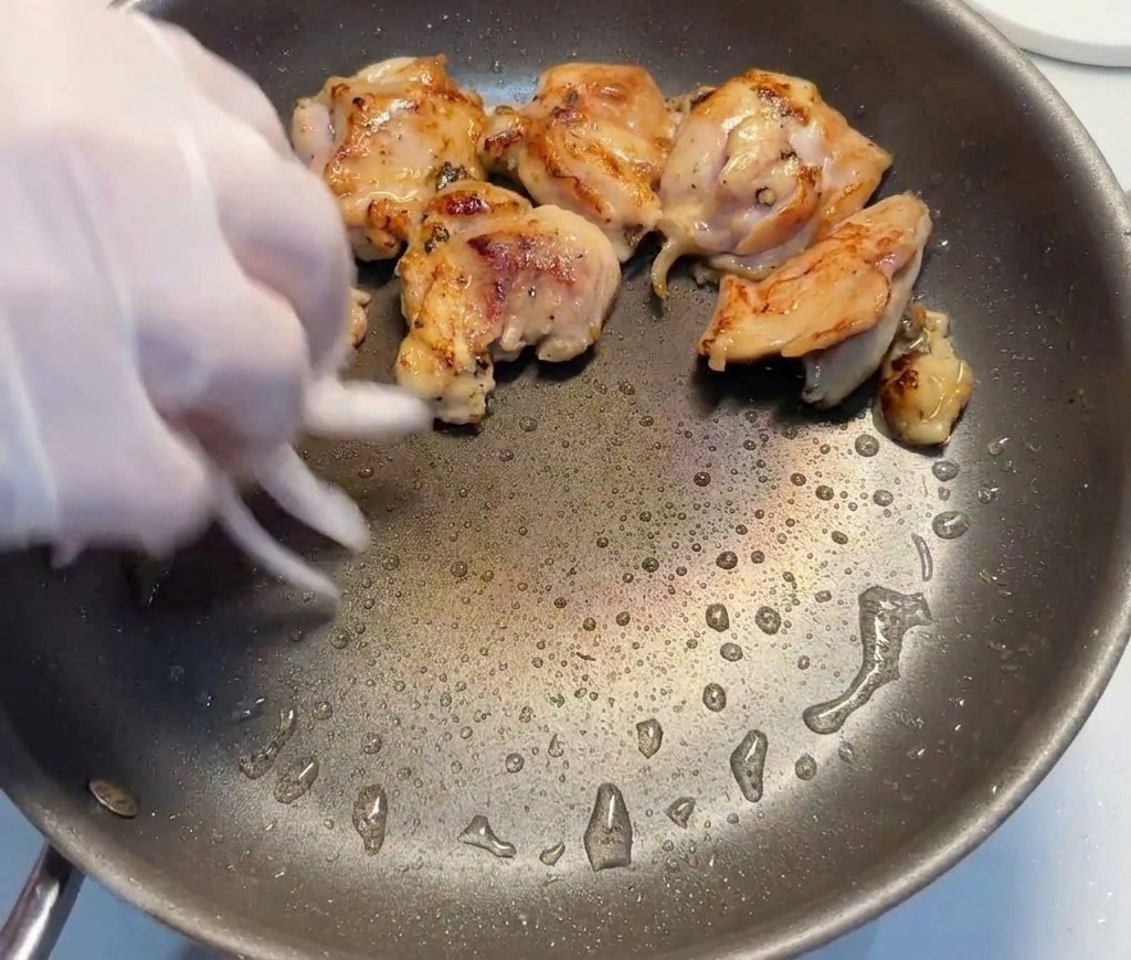 Rote Zwiebelstreifen werden zu den angebratenen Hähnchenstücken in die Pfanne gegeben.