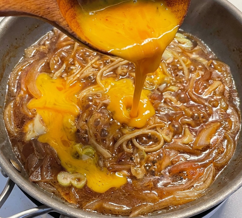 Verquirlte Eier werden über die Zwiebel-Lauch-Mischung in der Pfanne gegossen.