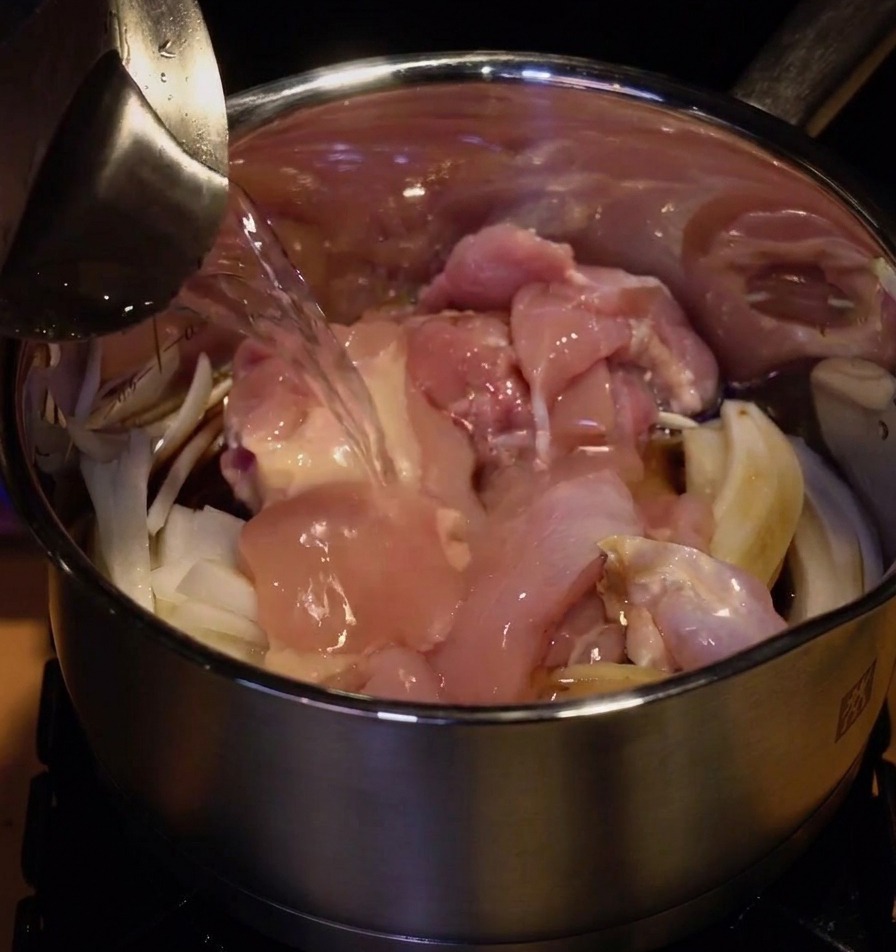 Wasser wird aus einem Krug in den Topf gegossen, bis Fleisch und Zwiebeln bedeckt sind.