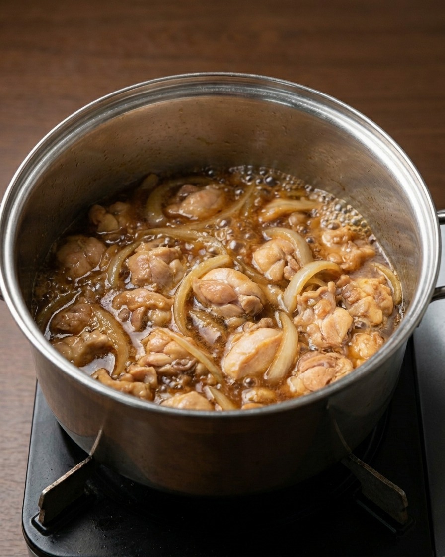 Hähnchen und Zwiebeln köcheln in einer dunkelbraunen, sprudelnden Sauce auf dem Herd.