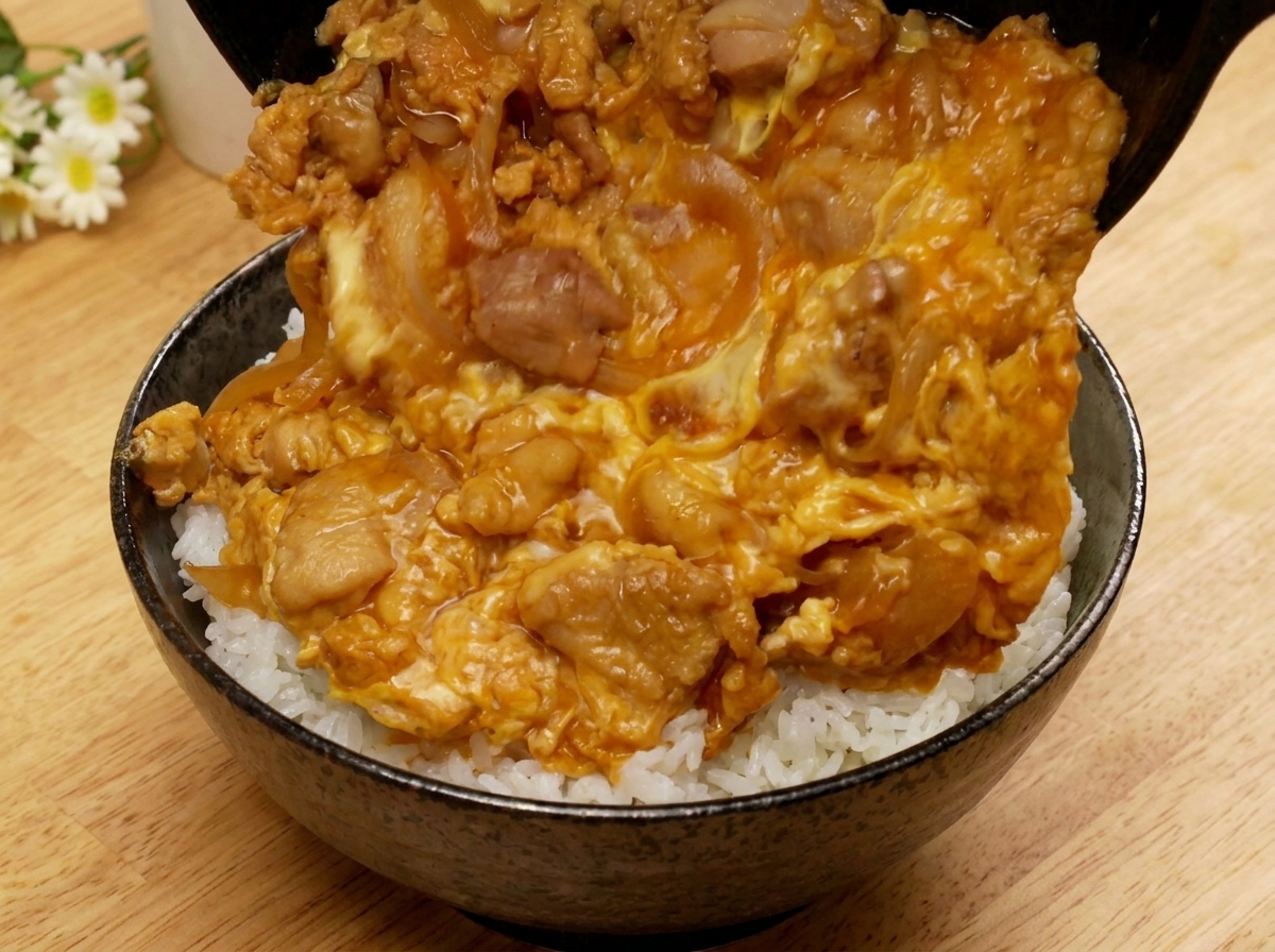 Die Pfanne wird gekippt, damit die Oyakodon-Mischung auf eine Schüssel mit weißem Reis gleiten kann.