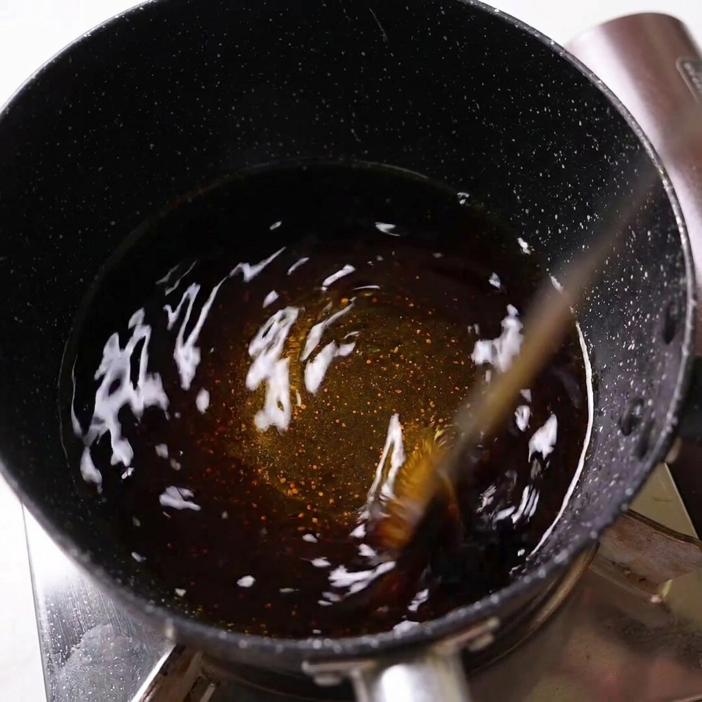 Dunkle Würzsauce wird in einem schwarz gesprenkelten Stieltopf auf dem Herd umgerührt.