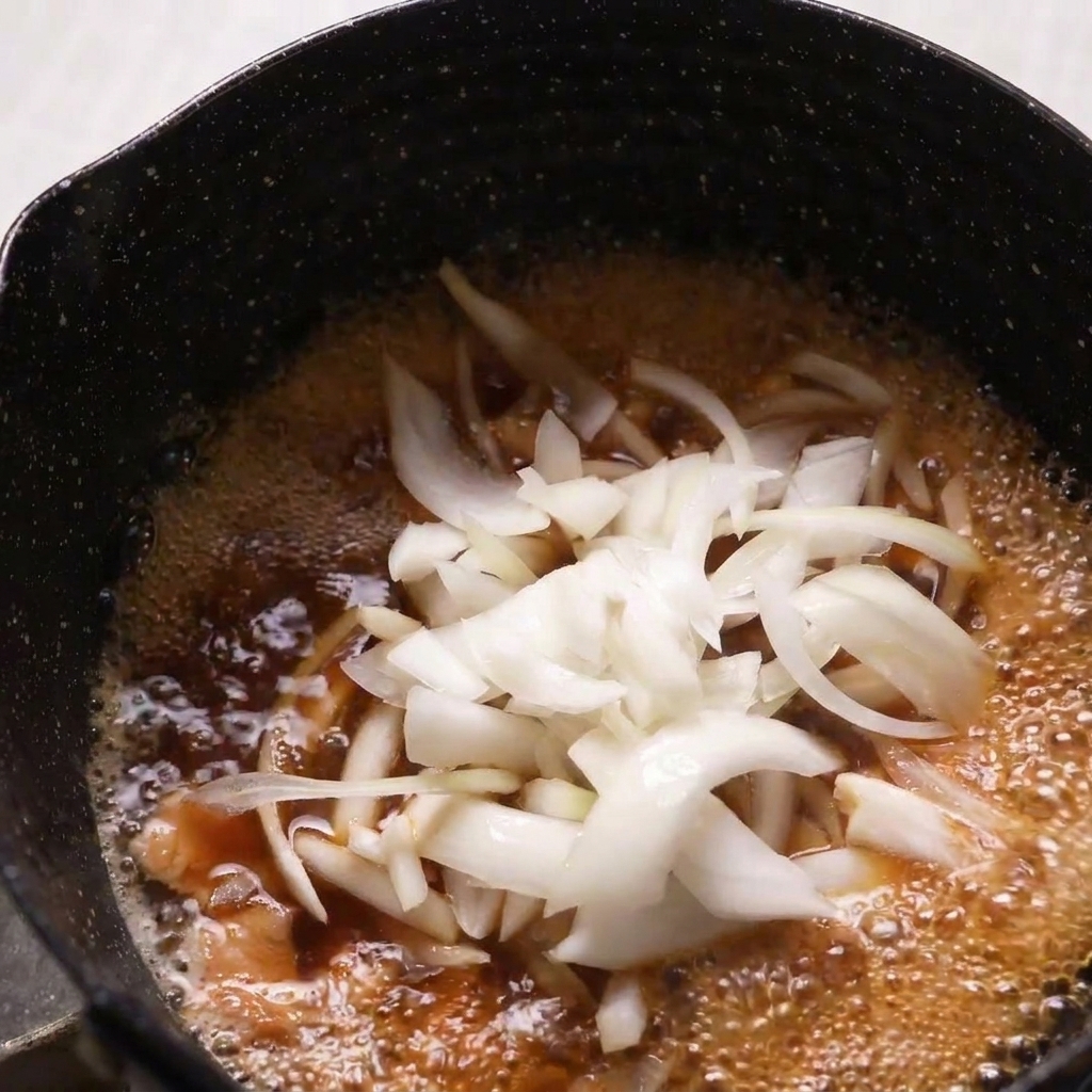 Fein geschnittene rohe Zwiebeln werden in eine köchelnde Pfanne mit Hähnchen und Dashi-Brühe gegeben.