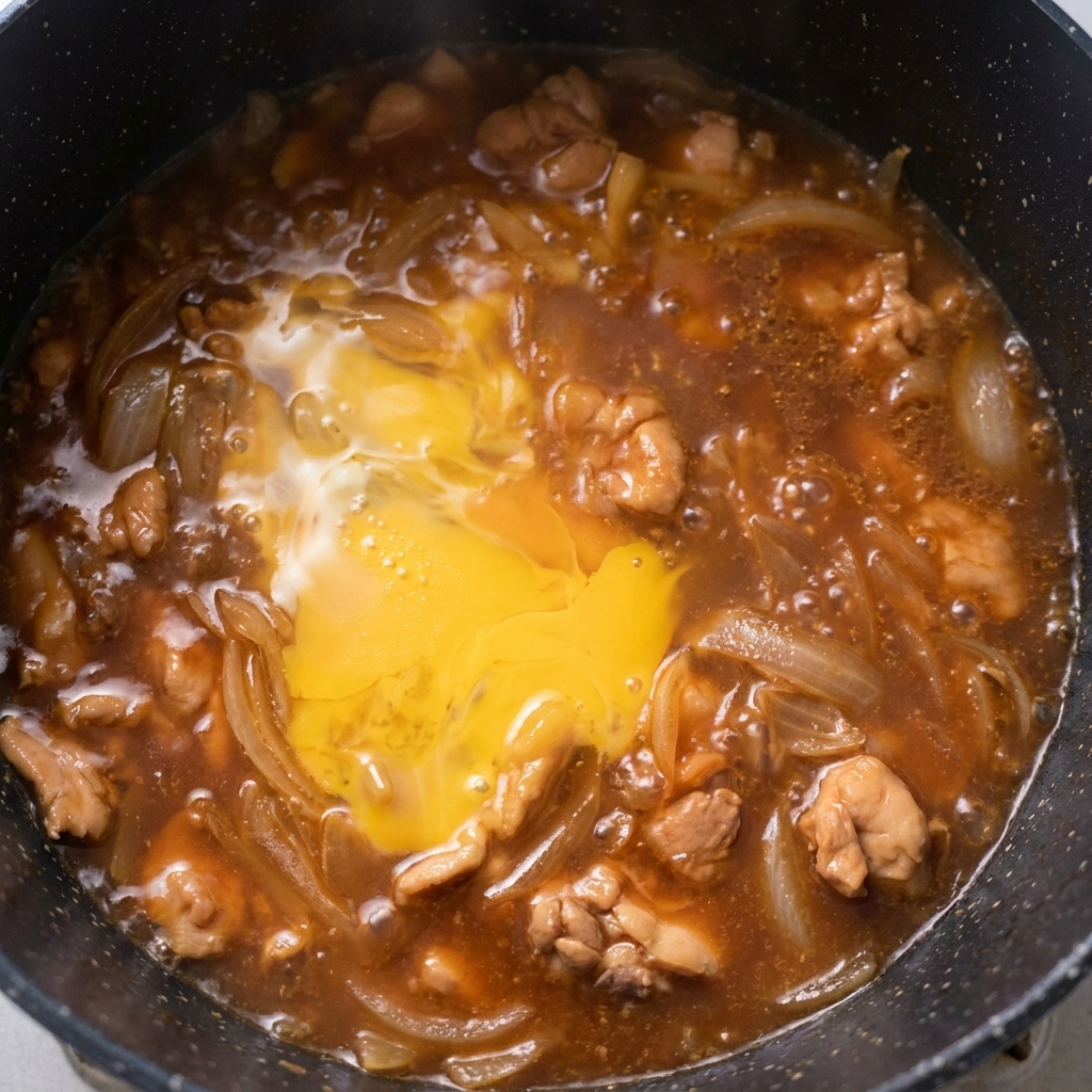 Eine teilweise gestockte Eischicht köchelt mit Hähnchen und Zwiebeln in der Pfanne.