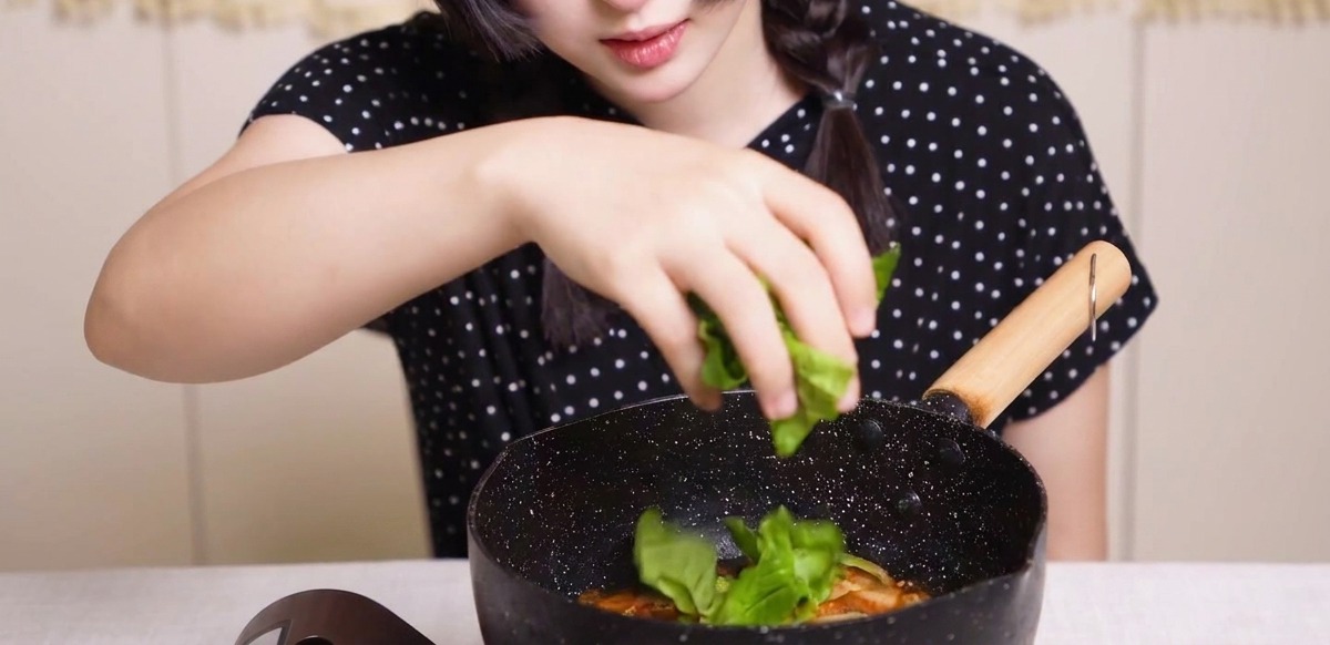 Frisches grünes Gemüse wird von Hand in die Pfanne mit Hähnchen, Zwiebeln und Ei gestreut.