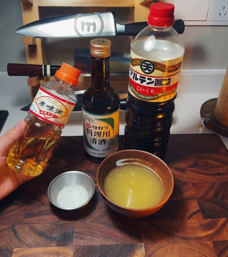 Anordnung von Mirin, Sake und Sojasauce neben einer Schüssel Hühnerbrühe und Zucker.