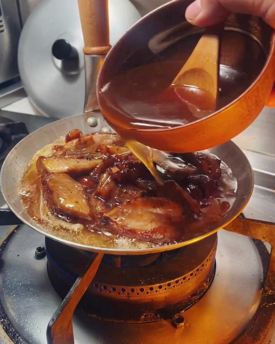 Eine dunkle Sauce wird aus einer Schale über Hähnchen und Zwiebeln in der Pfanne gegossen.