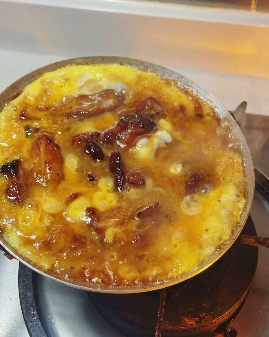 Oyakodon in einer Pfanne mit weich gestocktem, glänzendem Ei auf Hähnchen und Zwiebeln.