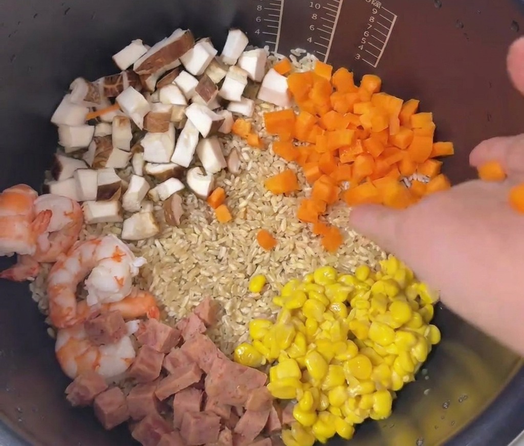 Eine bunte Anordnung aus Karotten, Mais, Fleisch, Pilzen und Garnelen liegt geschichtet auf dem Reis.