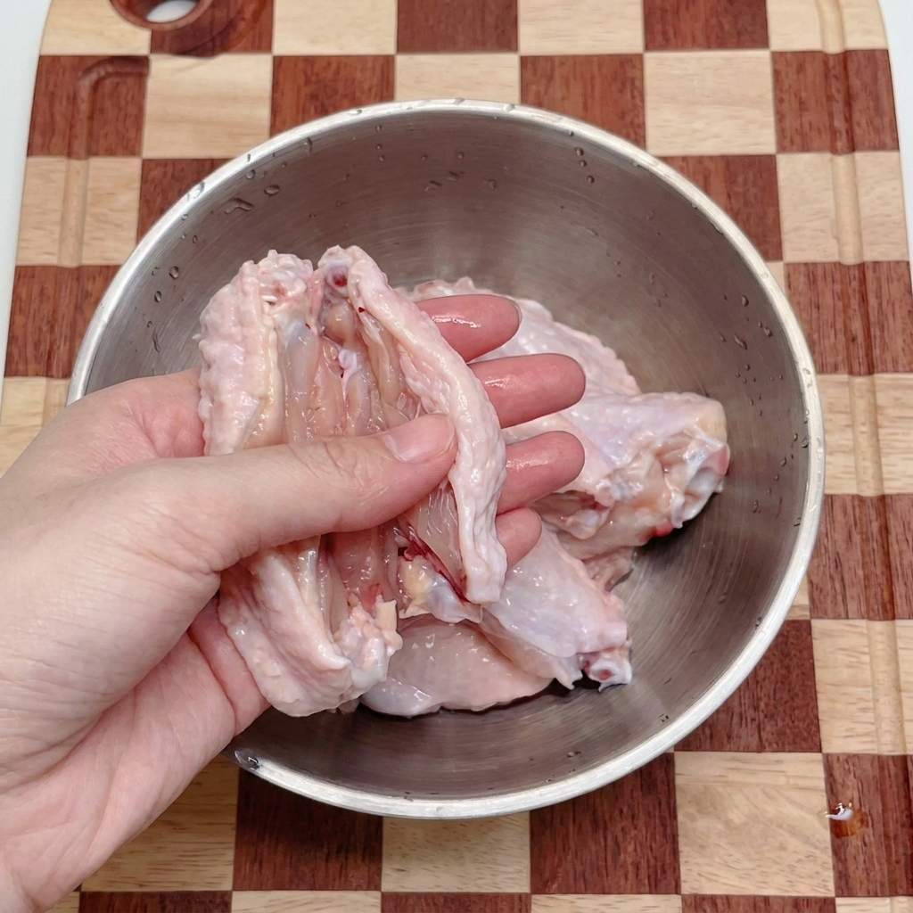 Hände schneiden rohe Hähnchenflügel mit einer Küchenschere in einer Edelstahlschüssel in zwei Teile.