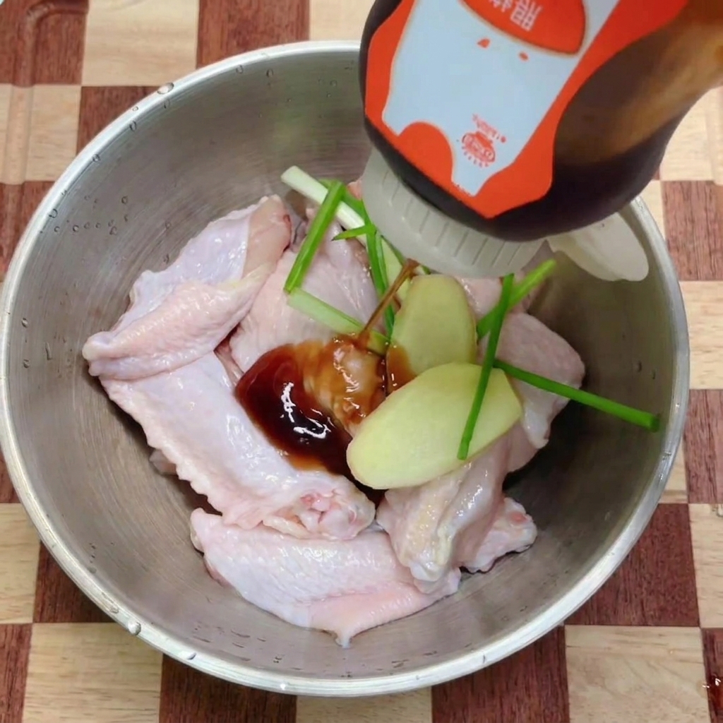 Dunkle Teriyaki-Sauce wird aus einer Flasche über rohe Hähnchenflügel mit frischen Kräutern gegossen.