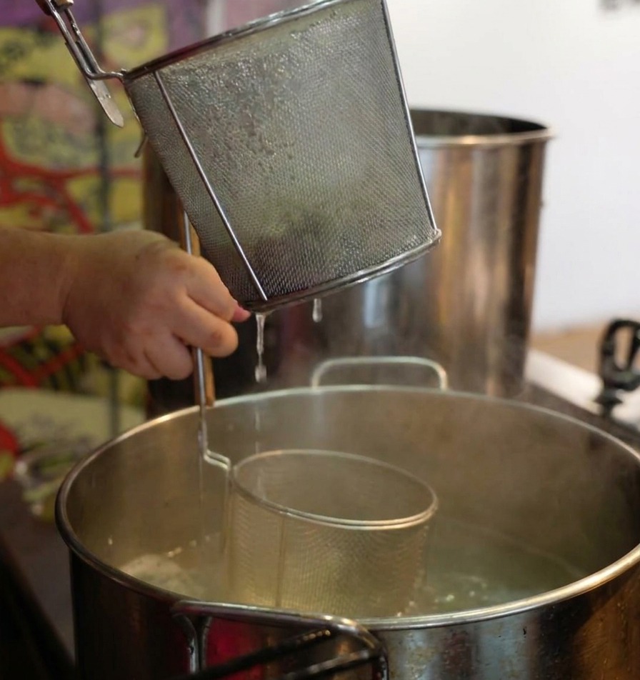 Hände halten ein hohes Nudelsieb über kochendes Wasser und schütteln es kräftig, um Nudeln abzutropfen.