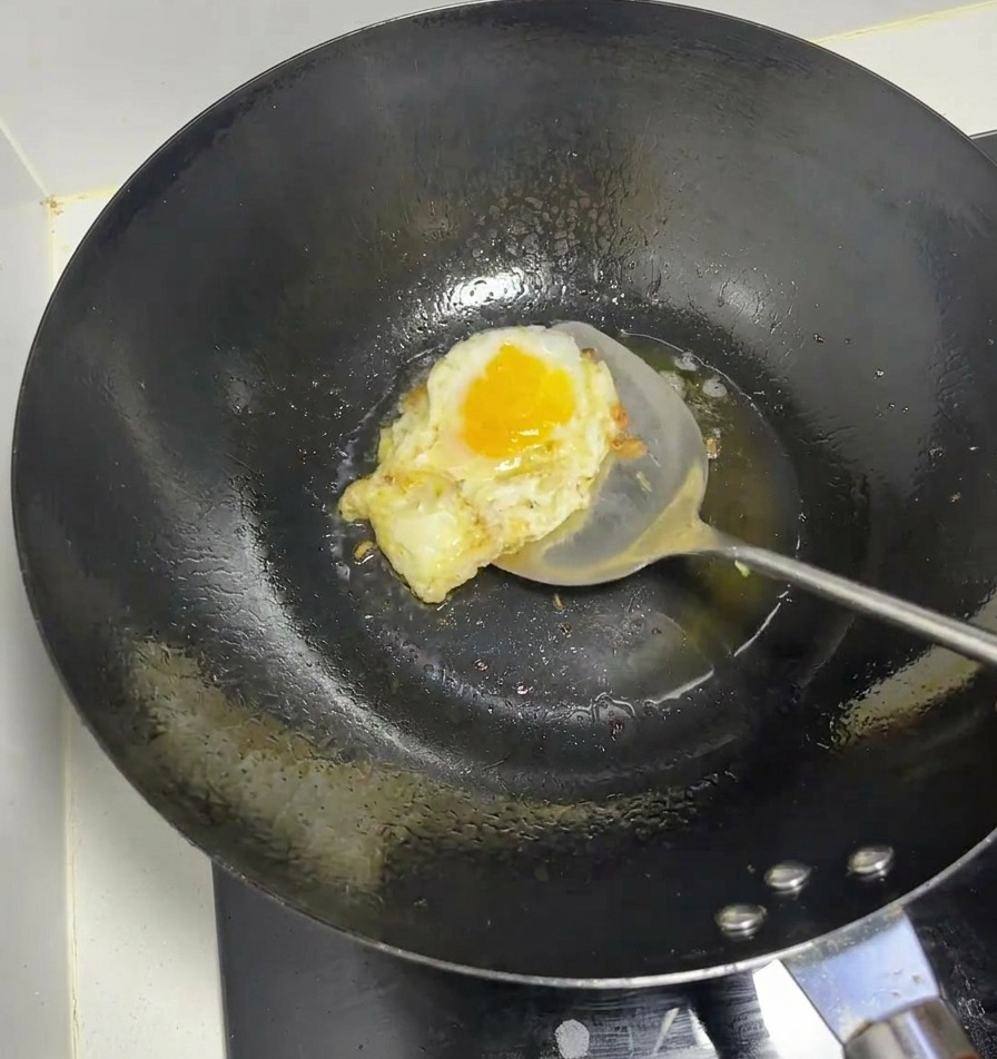 Ein Ei wird in einem heißen schwarzen Wok mit einem Metall-Pfannenwender gebraten.
