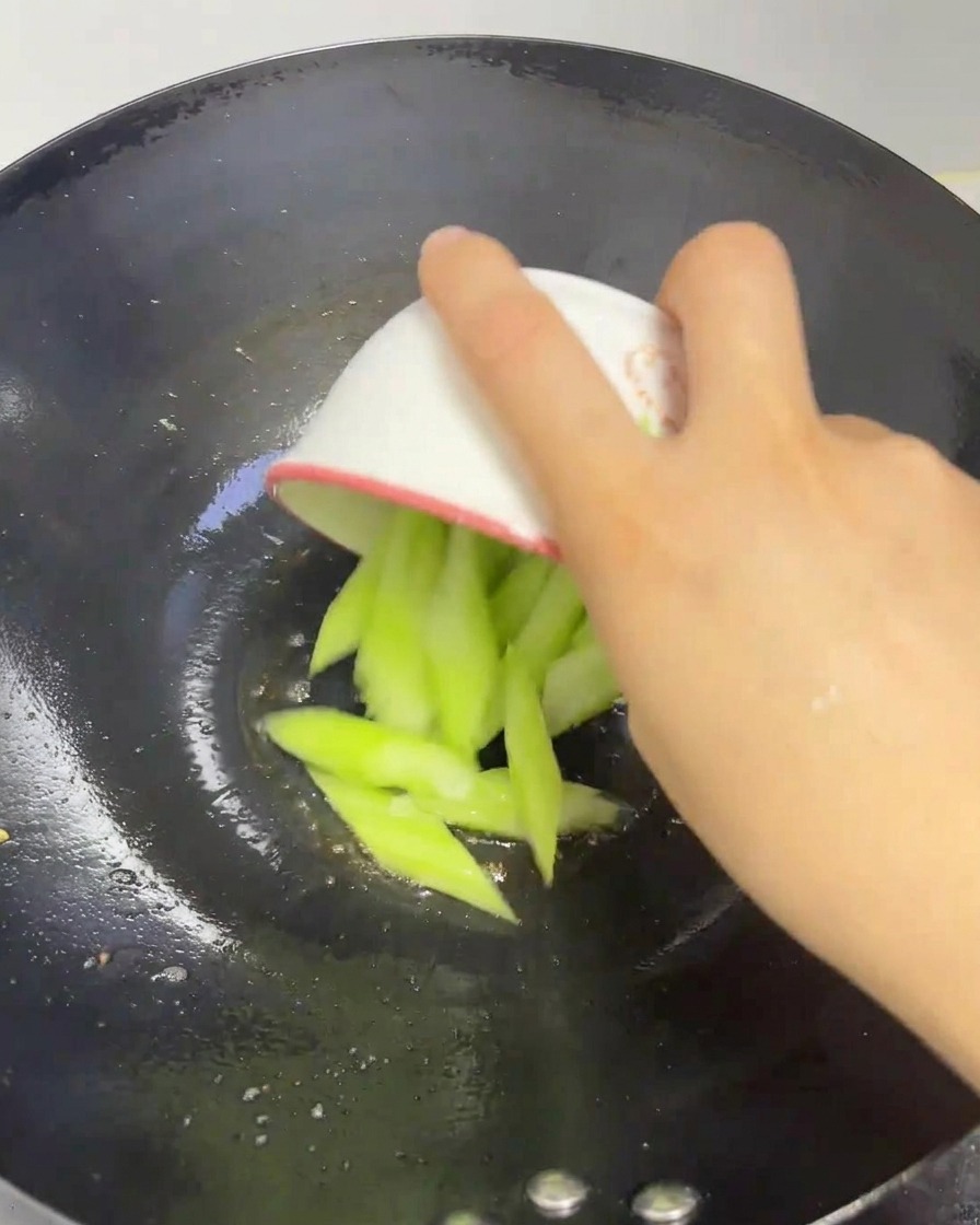 Frische grüne Seidenmelonenscheiben werden aus einer kleinen Schale in den erhitzten Wok gegeben.