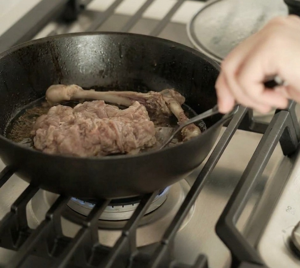 Die Entenkeule wird in der Pfanne gewendet und zeigt eine perfekt gebräunte, knusprige Haut.