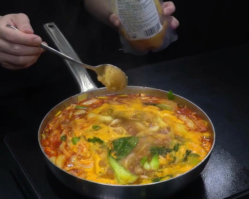 Ein Löffel mit gehacktem Knoblauch wird in eine Pfanne mit kochender roter Suppe gegeben.